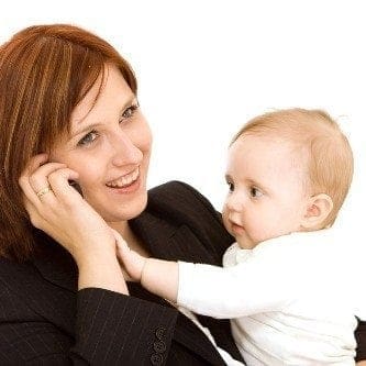 A woman holding a baby while talking on the phone, finding work-life balance as she balances her responsibilities as a parent and pursues job opportunities.