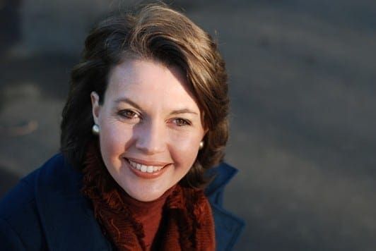 A working mum in a blue coat and scarf smiling, finding work-life balance.