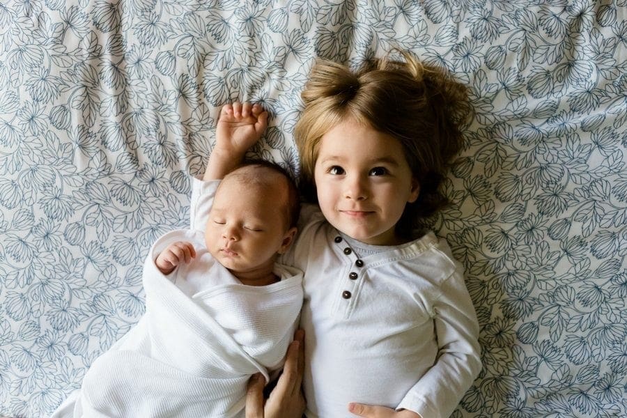 A baby and a toddler peacefully laying on a bed, showcasing the essential balance between parenting and work-life responsibilities.