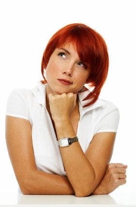A career-focused woman with red hair balancing work and life while leaning against a table.
