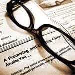A pair of glasses on top of a newspaper highlighting job opportunities.