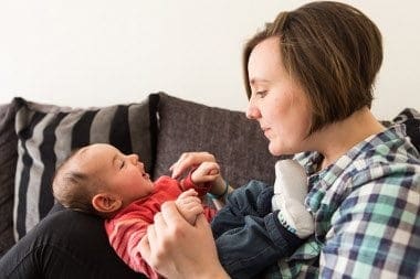 A mum holding a baby while sitting on a couch, exemplifying work-life balance for women returners.