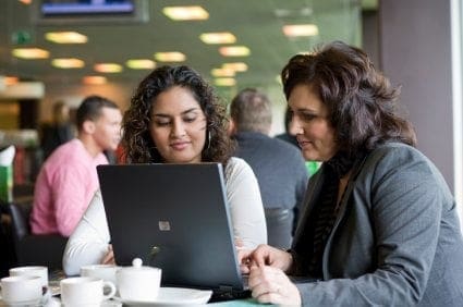 Two career women returners sitting at a table, working and looking at a laptop.