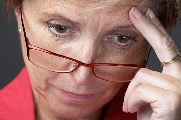 A working woman wearing glasses is holding her hand to her head.