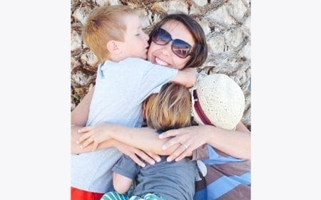 A mum is hugging her children in front of a tree.