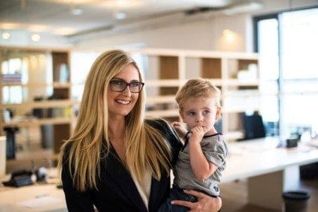 A working woman holding a child in an office.