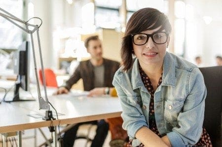 A woman in glasses sitting at a desk in an office, embodying the concept of women returners who are seeking job opportunities to restart their careers.
