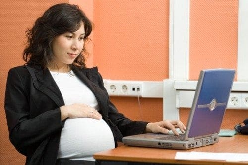 A career-driven woman sitting at a desk using a laptop, successfully balancing work and pregnancy.