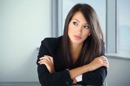 A career-driven woman in a business suit confidently leaning against a desk.