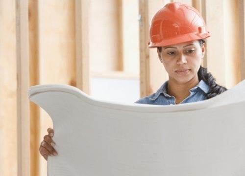 A career-driven woman in a hard hat confidently holding a blueprint.