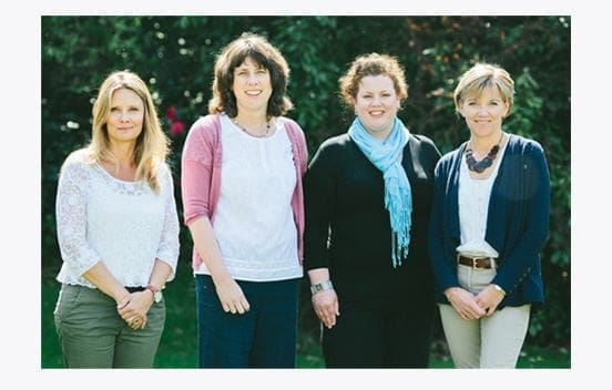 Four women standing next to each other, showcasing their strong career and job roles while posing in front of a tree.