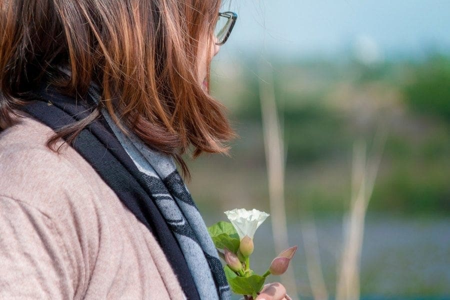 A woman peacefully holding a white flower near a body of water, finding work-life balance.