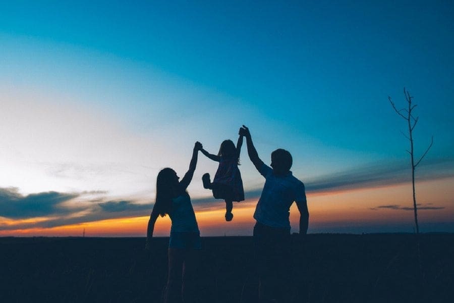 A silhouette of a family, including a mum, holding up their hands in the air at sunset.