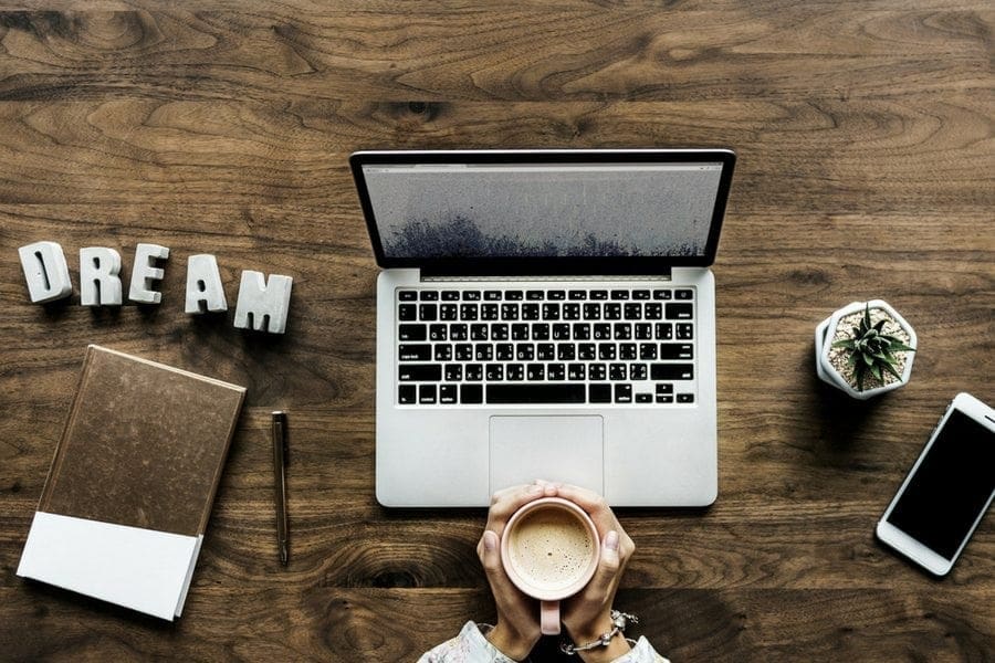 A person achieving work-life balance while holding a laptop and a cup of coffee on a wooden table.