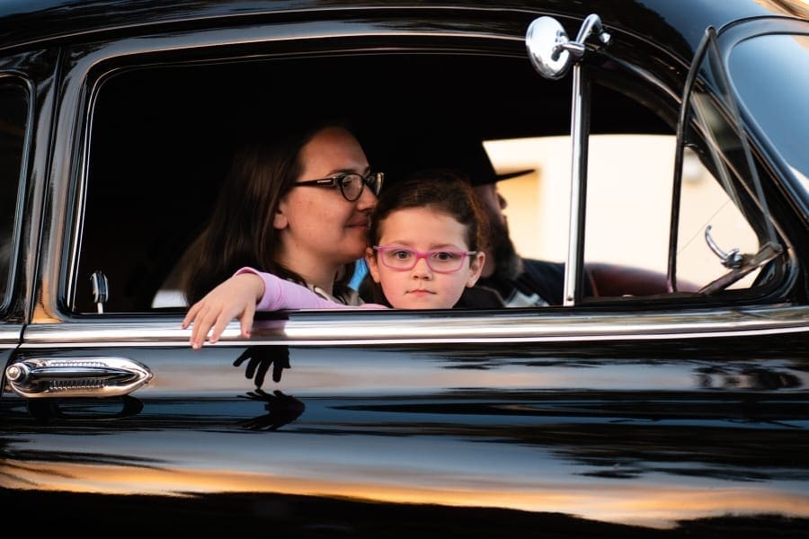 A working mother and her daughter sitting in the back seat of an old car.
