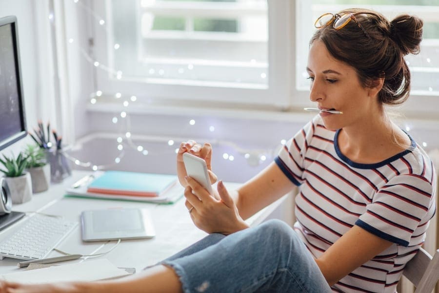 A career-focused woman multitasking, sitting in front of a computer and using a cell phone.