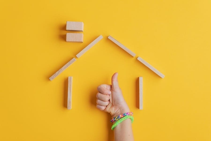 Mum working, hand making a house with wooden blocks on a yellow background.