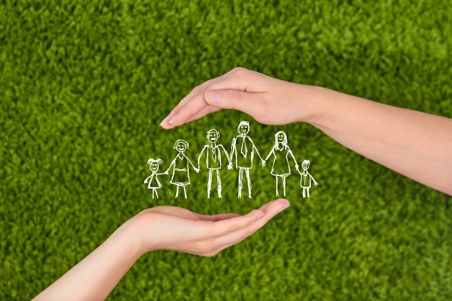 A mum's hand holding a drawing of a family on green grass.