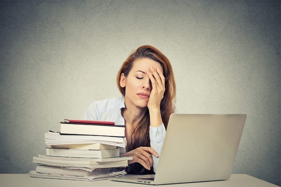 A multitasking woman finding work-life balance with a stack of books and a laptop.