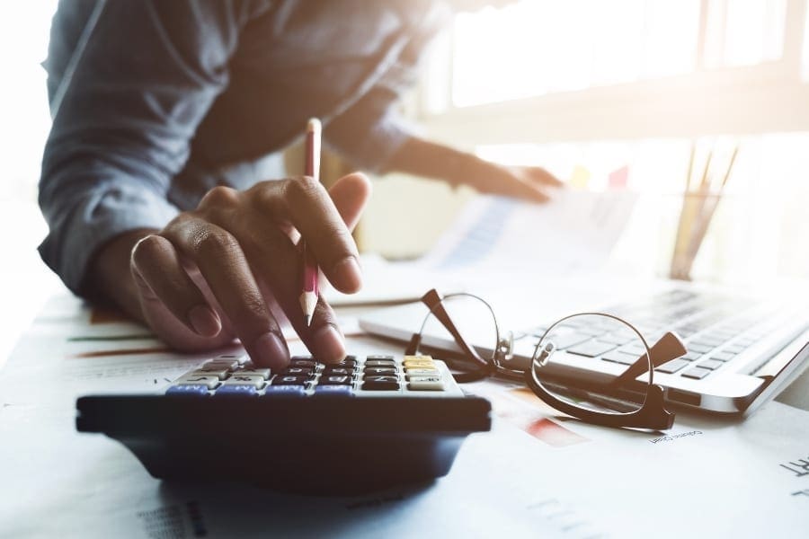 A man is working at his desk, calculating with a calculator.