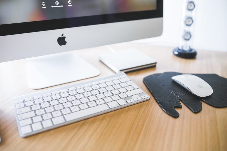 A desk setup with an Apple computer, mouse, and keyboard on a wooden surface.