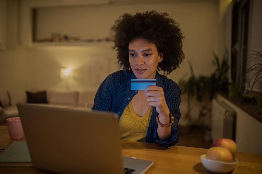 A woman utilizing a credit card while working remotely on her laptop.