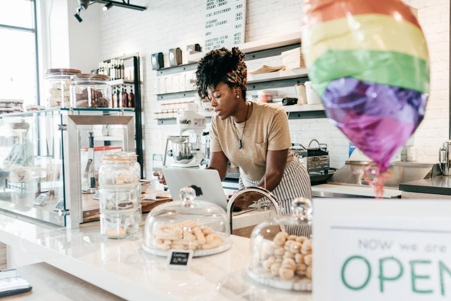 A mother working at a bakery counter with a rainbow balloon, balancing her career and family responsibilities.