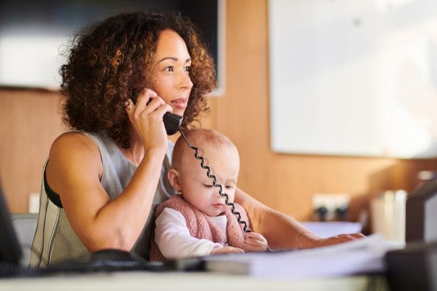 A working woman multitasking by talking on the phone while holding a baby, showcasing the challenges faced by women returners in managing personal and professional responsibilities.