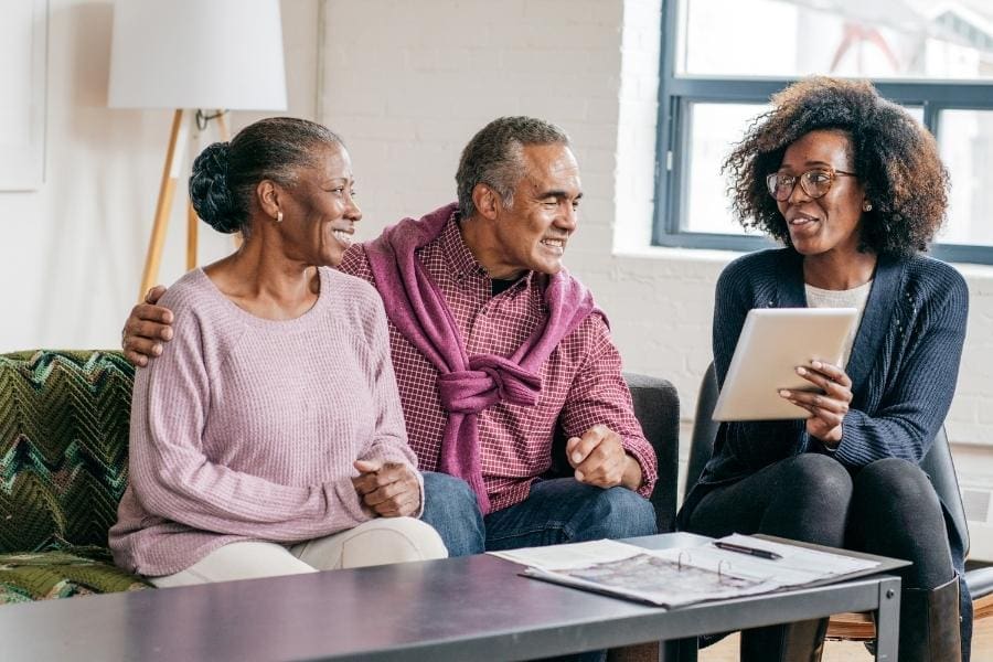 Three elderly people, including a mum, sitting on a couch looking at a tablet.