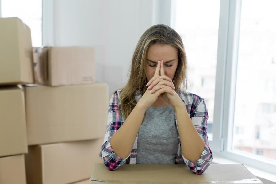 A woman utilizes 7 tips to make moving less stressful while sitting at a table amidst moving boxes.