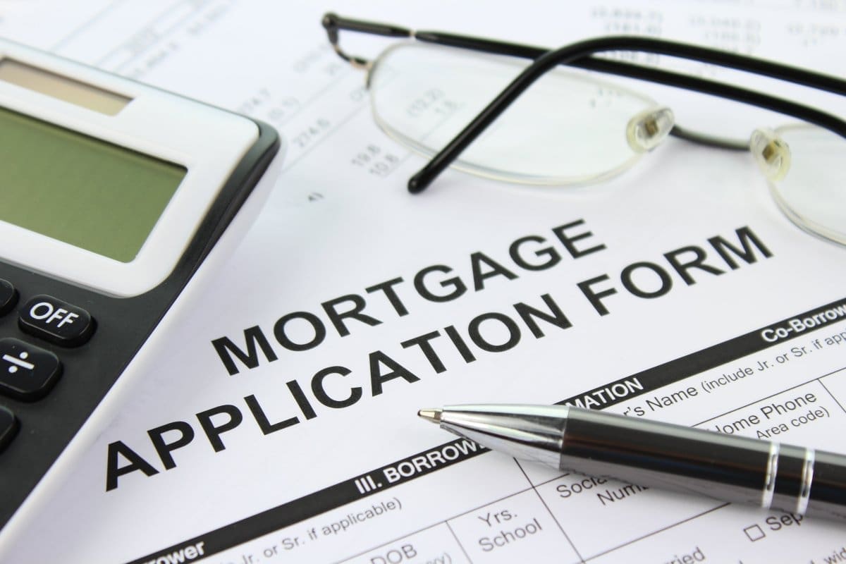 A mortgage application form on a desk with a pair of glasses, a calculator, and a pen placed nearby—everything a business owner needs for securing a mortgage.