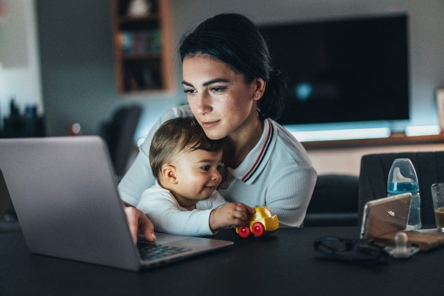 A woman is multitasking with a laptop and a baby, considering new careers after having a child.