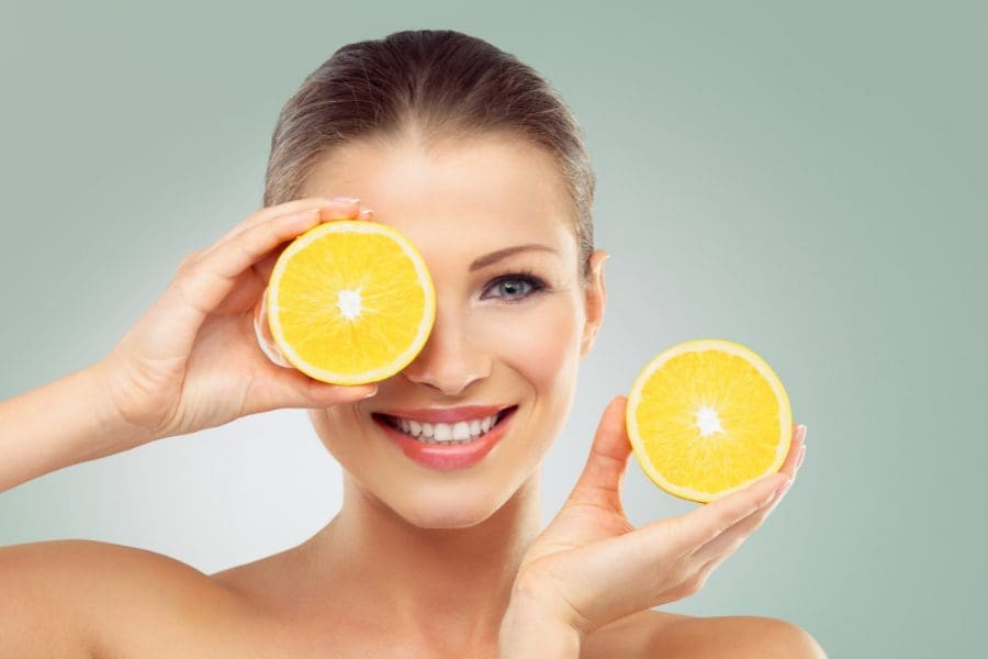 A busy parent holding a slice of orange in front of her eyes, learning how to care for her skin.