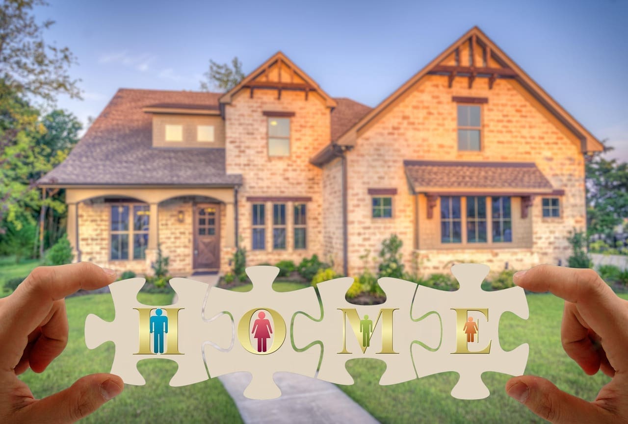 Hands hold four puzzle pieces spelling "HOME," with icons of a man, woman, and two children in front of a large suburban house under a clear sky—highlighting the importance of mortgage tips in home buying.