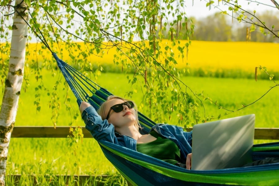 A calm woman finds solace in a hammock while using her laptop.