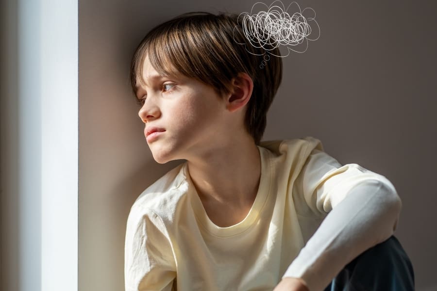 A young boy with brown hair looks out of a window, appearing thoughtful, with a scribble depicting confusion or stress above his head, illustrating the challenges of child school anxiety.