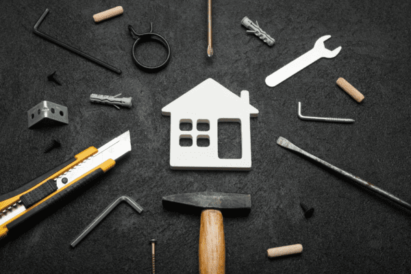 Various hand tools and hardware parts arranged around a white house-shaped cutout on a dark surface.