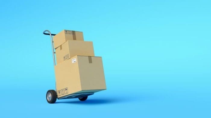 A hand truck loaded with three cardboard boxes, stacked in descending size order, against a plain blue background.