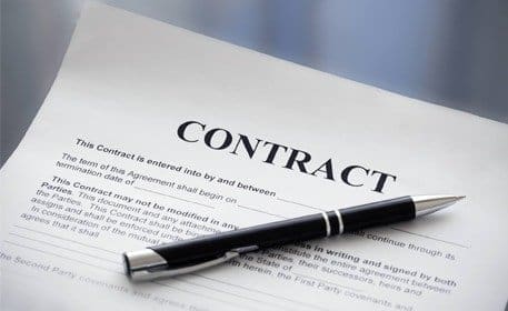 A black pen rests on a printed contract document, with the word "CONTRACT" prominently displayed at the top.