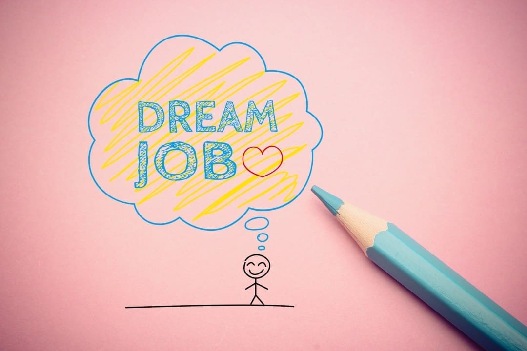 A drawing of a stick figure thinking of a cloud labeled "DREAM JOB" with a heart, next to a blue pencil on a pink background.
