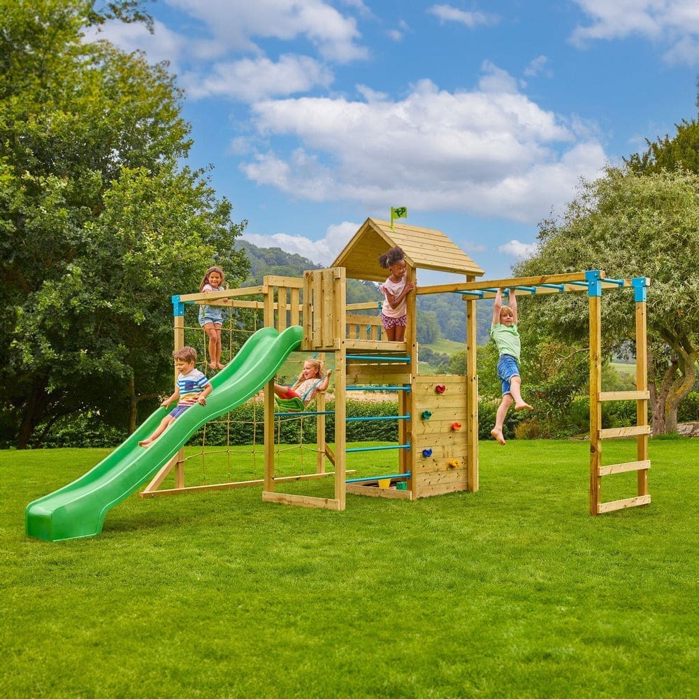 Five children play on a wooden outdoor playground set with a green slide, climbing wall, monkey bars, and a small tower on a grassy lawn.
